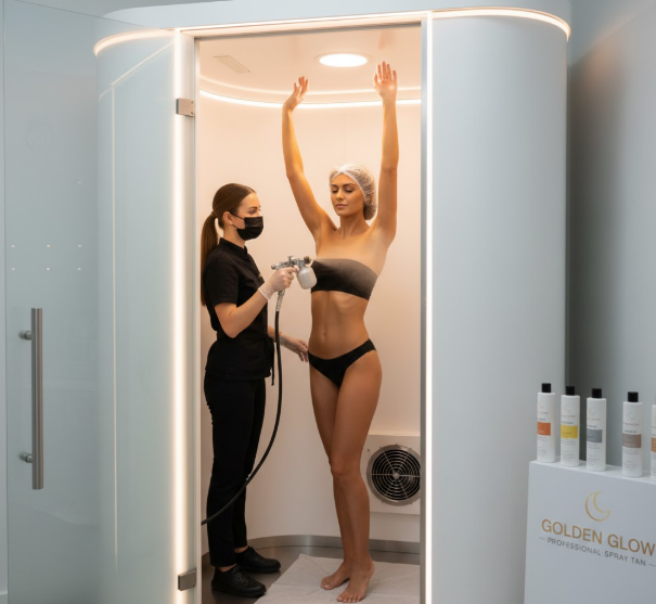 Professional spray tan booth with technician applying tan to client